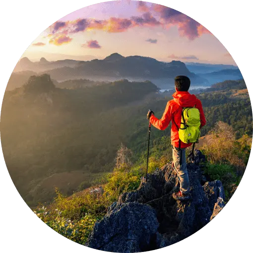 A man looks over a valley and neighboring hills from the top of a mountain.